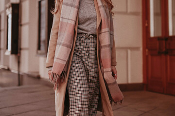 Poster - Female figure wearing beige long autumn warm coat, checkered pants and scarf. Outdoor street style fashion portrait