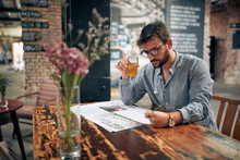 Young Man With Glasses And Casual Wear Reading Newspaper In Cafe, Sitting Alone.