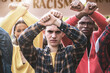 Youth Parade Against Racial Discrimination - Young people in a parade, three teens with crossed arms and clenched fists, surrounded by others holding anti-racial discrimination signs.
