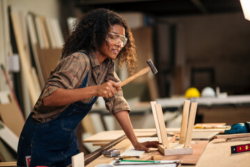 Small business owner young black female carpenter working a wood work in carpentry workshop. Young woman handcrafting and design chair for minimal home furniture.