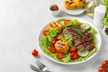 Wall Mural - Roast beef salad on white plate and grey background. Salad, meal with meat steak, grilled corn and beef meat with vegetable. Diet dinner concept.