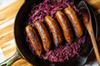 Beer-braised bratwurst sausages with red cabbage and onion in a cast-iron skillet.