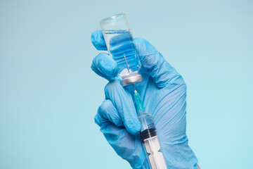 The doctor's hand wears a medical glove holding a syringe while taking a liquid vaccine from a vial about to be injected. Injection vaccination concept