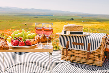 Wall Mural - Spring or summer picnic with croissants, fruits and rose wine on the meadow full of wildflowers.