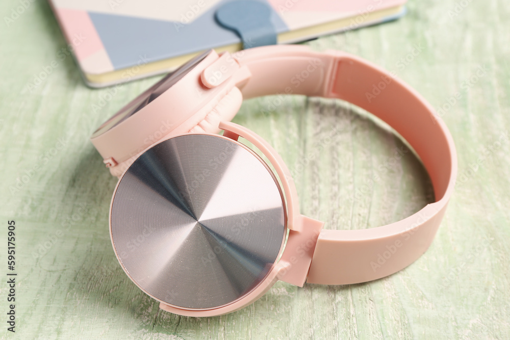 Headphones with notebook on green wooden background, closeup