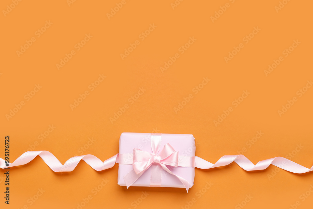 Gift box with beautiful bow and ribbon on orange background
