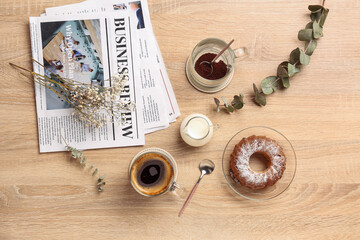 Wall Mural - Cup of coffee with milk, cake, newspapers and eucalyptus branches on light wooden background