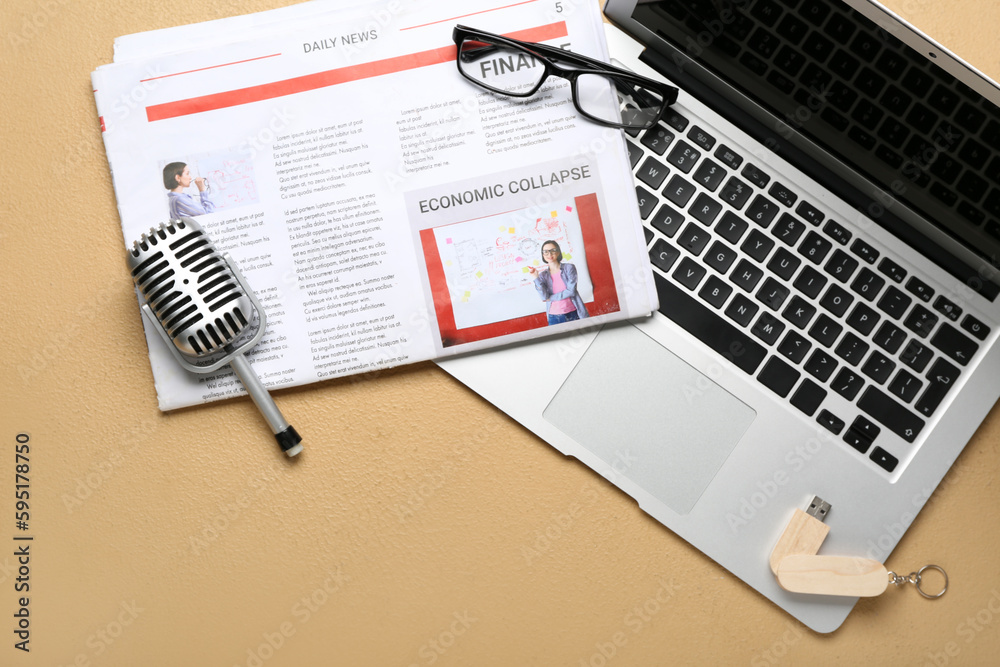 Newspaper with microphone, eyeglasses, USB flash drive and laptop on beige background
