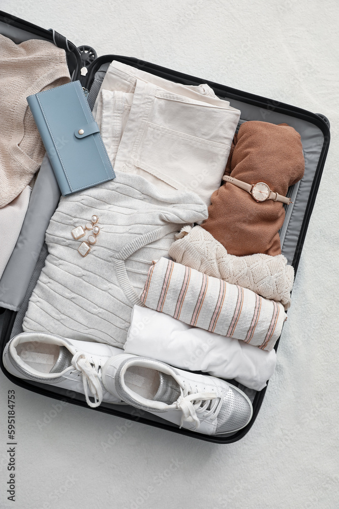 Suitcase with female clothes and accessories on white blanket