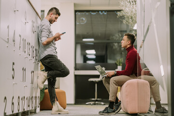 Good looking man scrolling on his phone after work while his male colleague is talking to him