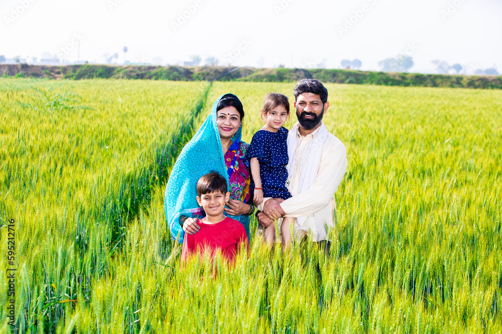 Portrait of happy young indian farmer family standing at wheat ...