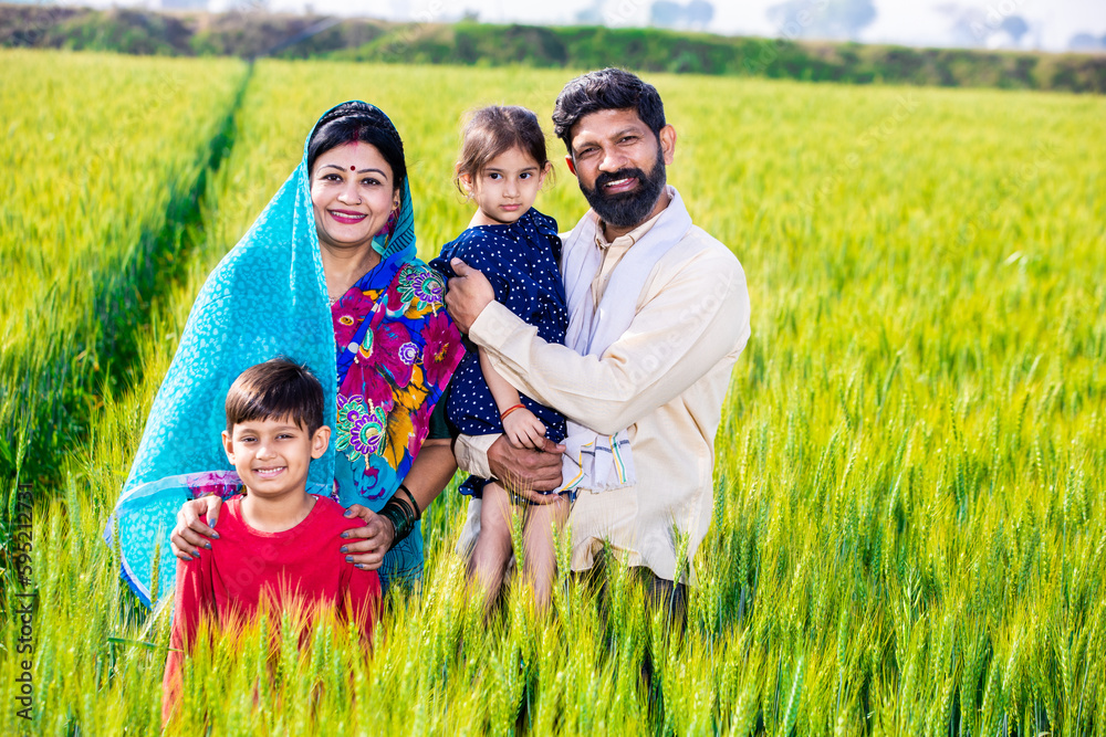 Portrait happy young indian farmer family standing at green wheat ...