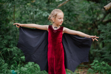 Wall Mural - Little girl with white hair in the form of a bat in the forest. Halloween costume for a child. Waiting for a party