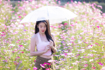 Wall Mural - Beautiful woman happy traveler holding umbrella and walking in the flowers garden. Young woman smile and relaxing in flower garden. Woman's hand touching and enjoying cosmos flowers.Travel concept.