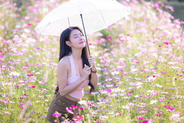 Wall Mural - Beautiful woman happy traveler holding umbrella and walking in the flowers garden. Young woman smile and relaxing in flower garden. Woman's hand touching and enjoying cosmos flowers.Travel concept.