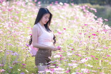 Wall Mural - Beautiful woman happy traveler walking in the flowers garden. Young woman smile and relaxing with happy  around outdoor garden. Woman's hand touching and enjoying beauty cosmos flowers.Travel concept.