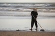 Male in a sun hat working with a rake cleaning a polluted beach