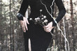 © junky_jess - Beautiful faceless woman in black tight dress with dried flowers in hands in the black forest, film grain, effect of an old photo, selective focus.