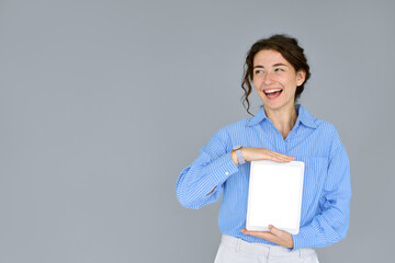 Happy smiling business woman holding digital tablet computer showing blank empty mock up screen looking aside advertising software, website or web service standing isolated on gray background.
