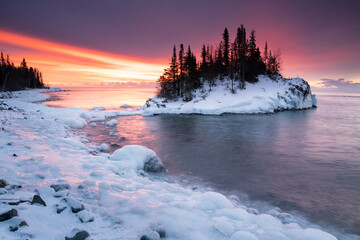bright warm sunrise behind frozen island and lakeshore