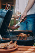 © gstockstudio - Close-up of two people barbecuing meat on grill outdoors together