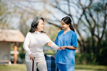 Asian young caregiver nurse support senior older male walking outdoors. Specialis doctor help and take care of elderly mature. Nursing home hospital garden