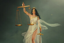 Portrait Fantasy Woman Greek Goddess Of Justice Themis Holding Scales And Sword In Hands. White Silk Vintage Dress Old Antique Style Flies Waving In Wind. Blind Girl Queen Eyes Blindfolded. Art Photo