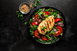 Chicken breast fillet grilled and fresh vegetable green salad with arugula, tomatoes and olives on black background, healthy food, mediterranean diet, top view