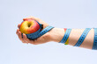 Jabłko trzymane w dłoni  na jasnym tle owinięte centymetrem krawieckim do mierzenia obwodów 