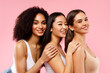 Young pretty asian, caucasian and black women posing together and smiling at camera, standing on pink background