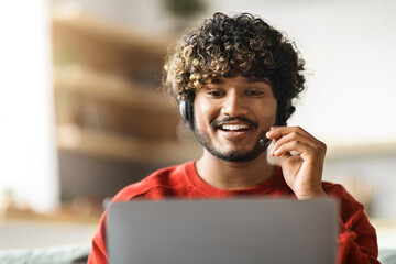 Sticker - Telecommuting Concept. Young Indian Male Wearing Headset Working On Laptop At Home