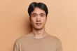 © WHstudio Leushin N - Portrait of serious dark haired adult Asian man with neutral facial expression focused at camera dressed in casual jumper isolated over brown background. Handsome Japanese guy poses in studio