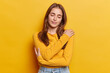 Calm millennial girl embraces own body cuddles herself has eyes closed wears casual jumper jeans isolated over yellow background pleasantly feels comfortable poses. Tenderness and self esteem concept