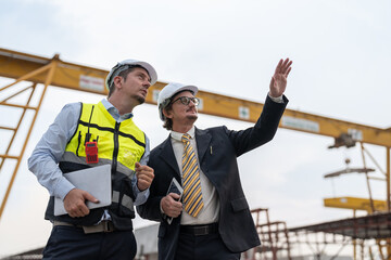 Businessman and male engineer discussing the project making precast concrete wall at construction site.