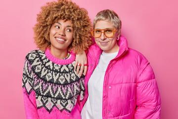 Wall Mural - Studio shot of cheerful young European women meet together wear jumper and jacket stand next to each other feel happy isolated over pink background. Fashionable female models pose in studio.