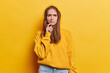 Displeased sulking brunette woman frowns face has dissatisfied expression purses lips wears casual hoodie thinks about solving problem isolated over vivid yellow background. Hmm let me think about it