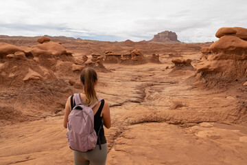 Woman hiking next to unique eroded Hoodoo Rock Formations at Goblin Valley State Park in Utah, USA, America. Sandstone rocks called goblins which are mushroom-shaped rock pinnacles. Canyon hike trail