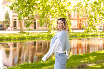 Wall Mural - Portrait of beautiful woman smiling and turn around in park at sunny day. Outdoor portrait of a smiling curly blonde girl. Happy cheerful girl laughing at park wear sweater, white longsleeves, shorts