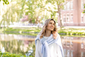 Wall Mural - Portrait of beautiful woman smiling and look at side in park at sunny day. Outdoor portrait of a smiling curly blonde girl. Happy cheerful girl laughing at park wear sweater, white longsleeve, short. 