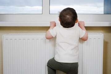 Toddler baby climbs to the window near the heating battery. A small child tries to climb on the windowsill. Kid aged one year eight months