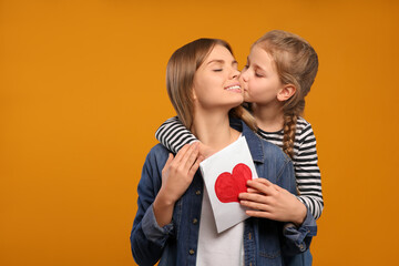 Wall Mural - Little daughter congratulating her mom with postcard on orange background, space for text. Happy Mother's Day