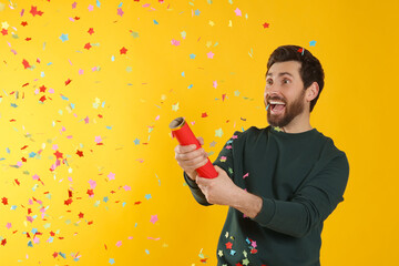 Emotional man blowing up party popper on yellow background