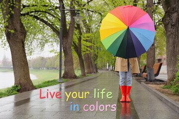 Live your life in colors, affirmation. Woman with rainbow umbrella walking in park on spring day