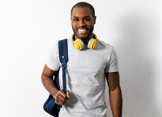 A dark-skinned man poses on a white background with headphones and a backpack. The man has a happy, apt, happy expression with the exam grades.