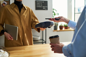 Poster - Close-up of clerk with terminal over counter desk and female client with smartphone during contactless payment for coffee in cafe