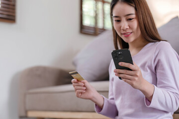 Wall Mural - young woman buying online with credit card and smart phone sitting on couch at home