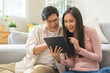 © KMPZZZ - Happy excited, smiling asian young couple love using tablet pc, great deal or business success, received or getting cash back, tax refund, good news by mail while sitting on sofa, couch at home.