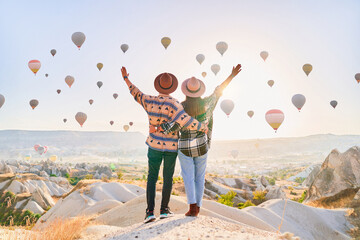 Sticker - Happy traveling couple with open arms standing together in valley in Anatolia, Kapadokya. Flying hot air balloons at beautiful destination in Nevsehir, Goreme
