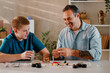 © Zamrznuti tonovi - Happy son and his smiling father playing together at the dinning table at home.