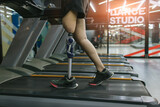 Fototapeta Tulipany - Sports woman with artificial leg running on treadmill at gym. Woman with prosthetic leg using walking on treadmill while working out in gym.